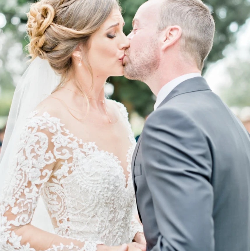 Baiser des mariés, la mariée en robe de dentelle brodée et voile, chignon tressé