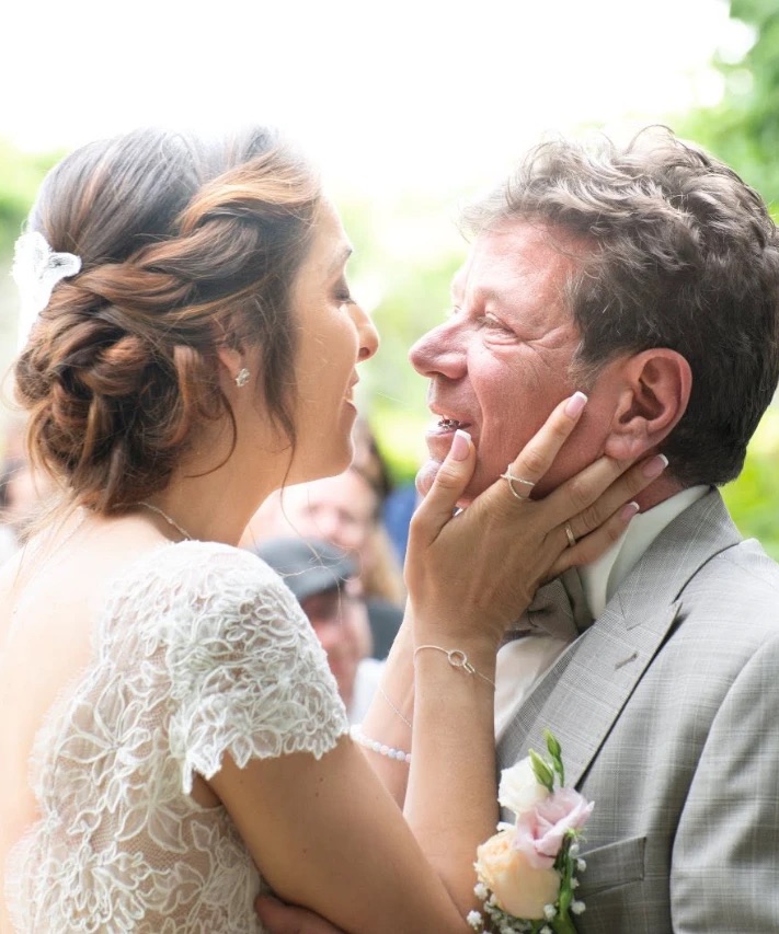 La mariée prend le visage de son mari entre ses mains, tous deux rient au milieu des invités